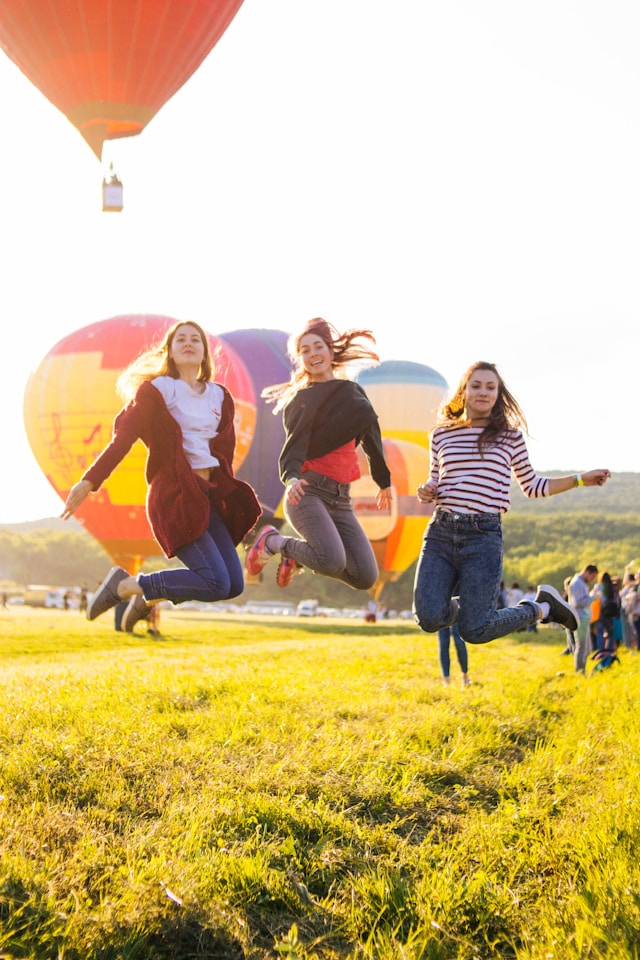 Three friends jumping with hot air balloons in the background